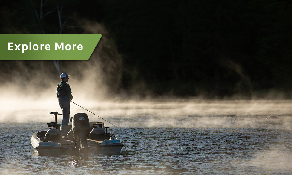 A man fishing on a motorboat with the early morning fog.